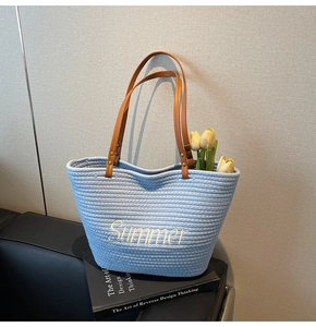 Close-up of light blue straw tote with Summer embroidery and brown leather handle
