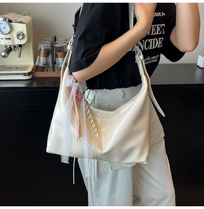 Close-up of cream white leather hobo bag with lace bow and pink heart charm