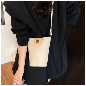 Detailed shot of cream bucket bag with lychee texture and gold clasp worn by a model