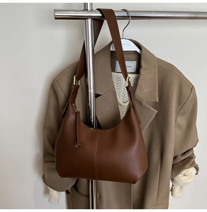 Close-up of a brown leather shoulder bag hanging on a metal rack with a beige suit