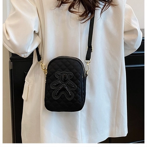 Detail of black quilted crossbody phone bag with sequin bear patch on white blazer