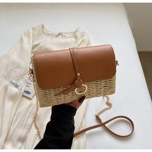 Close-up of woven straw crossbody bag featuring brown leather flap and gold ring buckle
