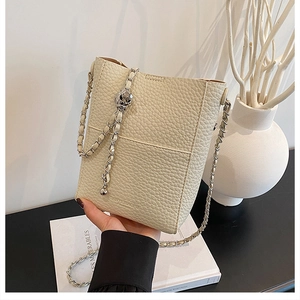 Close-up of beige lychee grain bucket bag featuring a silver metal chain and round charm