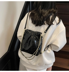 Detail of black quilted bucket bag featuring glossy finish and gold chain straps