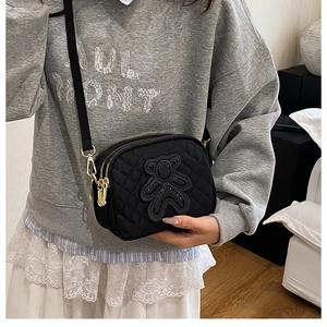 Detail view of black quilted crossbody bag with double zippers and cute bear patch
