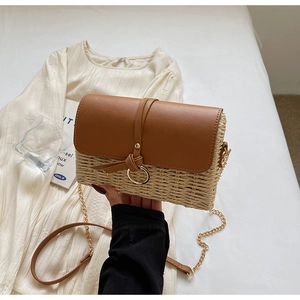Detail of woven straw shoulder bag with brown leather flap and metal ring closure