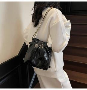 Sac seau matelassé en cuir verni noir avec chaîne dorée porté par un mannequin