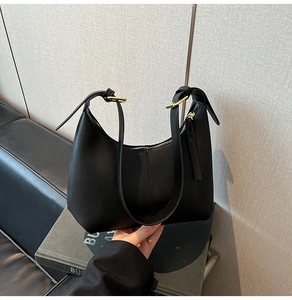 Detail of a matte black hobo shoulder bag featuring vertical stitching and a metal buckle