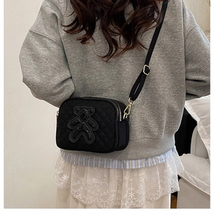 Rear view of a black quilted crossbody bag with sequined bear patch on a model