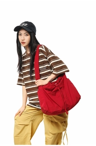 Détail du grand sac bandoulière rouge à cordon avec une tenue streetwear et une casquette