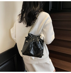 Détail de la texture brillante du sac seau matelassé et de la bandoulière chaîne