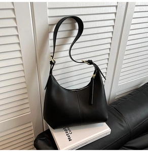 Detail of black crescent hobo bag with gold zipper and adjustable strap on a book