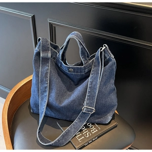 Detail of blue denim tote bag showing white contrast stitching and silver metal buckle