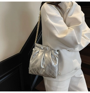 Detail of silver quilted bucket bag with gold chain strap shown on a model