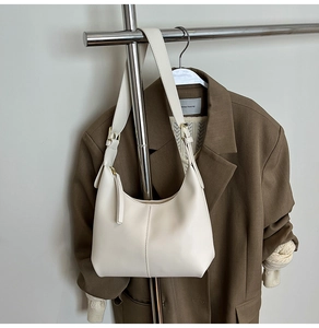 Detail view of cream leather hobo bag with gold hardware on a brown blazer background