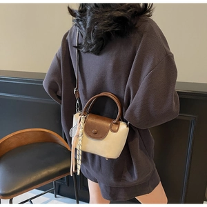 Detail of a two-tone mini crossbody bag with dark brown flap and woven knot charm