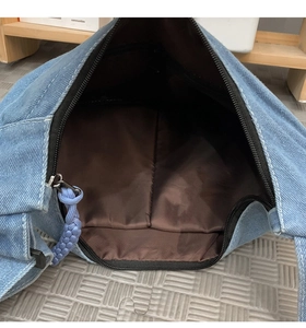 Detail view of denim shoulder bag interior with brown lining and woven zipper pull