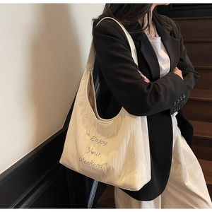 Detail of cream canvas tote bag with Enjoy Your Weekend embroidery on a model