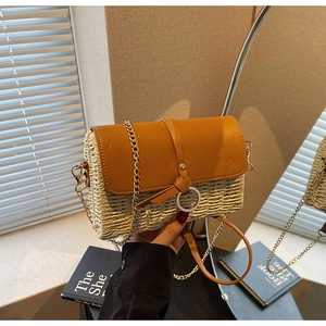 Detail of a straw woven crossbody bag with brown leather flap and gold chain strap