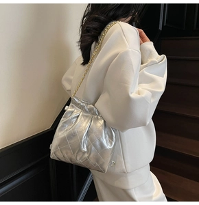Detail of silver quilted shoulder bag with drawstring closure and golden chain strap