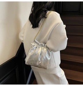 Silver quilted bucket bag with gold chain strap shown on model in modern interior