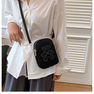 Detail of black quilted crossbody phone bag featuring a cute bear patch and dual zippers