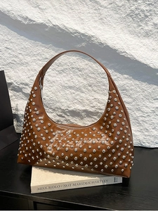 Brown PU hobo bag with silver rivets on a vintage book with a white stone wall backdrop