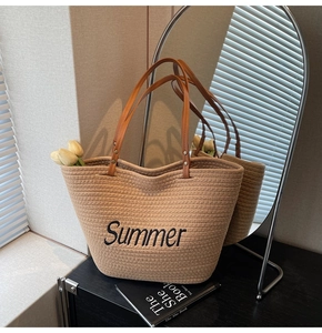 Détail d'un sac cabas en paille d'été avec broderie noire et poignées en cuir marron