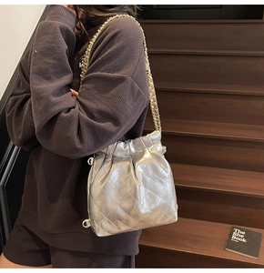 Sac seau matelassé argenté avec bandoulière dorée porté par un mannequin sur escalier