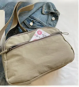 Detail of khaki nylon crossbody bag with front zipper pocket on denim background