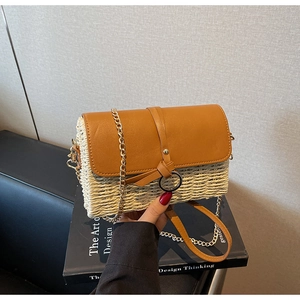 Detail of straw woven crossbody bag with brown leather flap and gold chain strap
