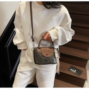 Detail of retro small crossbody bag in dark grey and brown with woven tassel charm