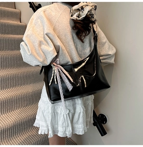 Detail of black glossy hobo bag featuring white lace trim and pink ribbon decoration