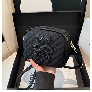 Detailed close-up of a black quilted crossbody bag with sequined bear and gold zippers