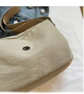 Detail shot of beige nylon crossbody bag showing soft texture and metal logo