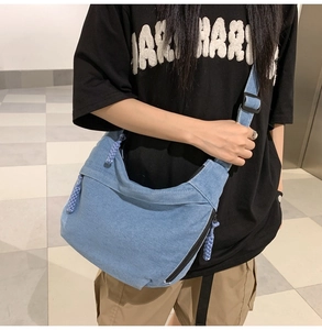 Detail of light blue denim crossbody bag featuring woven rope zipper and adjustable strap