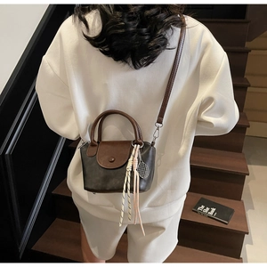Detail of a mini two-tone crossbody bag featuring a tennis racket charm and a slim strap