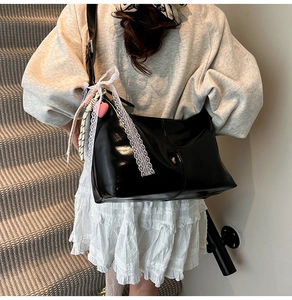 Detail of black patent leather hobo bag with pink heart charm and white lace ribbon decor