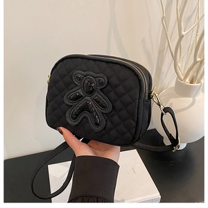 Close-up of black quilted crossbody bag featuring sequined bear patch and dual zippers