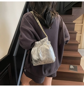 Silver quilted bucket bag with metal chain strap shown as a crossbody on a model