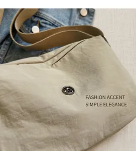 Close-up of khaki nylon pillow bag with round metallic logo and wide woven shoulder strap