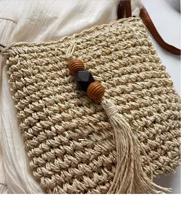 Dettaglio borsa in paglia intrecciata con perline in legno, nappe e tracolla in pelle marrone