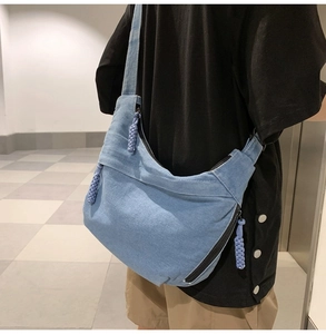 Detail view of light blue denim crescent shoulder bag with woven zipper pull on model