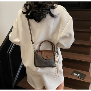 Detail view of retro crossbody bag with contrast handle and tassel on wooden steps