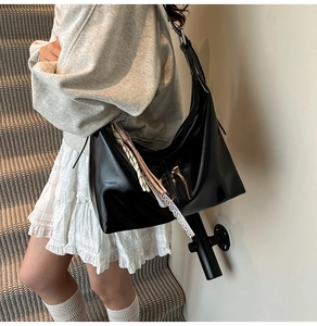 Detail of a black leather crossbody bag with lace ribbon and woven strap on model