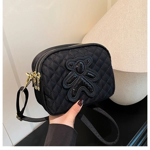 Detail of black quilted shoulder bag featuring sequin bear ornament and triple-zip pockets