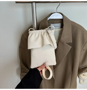 Détail du mini sac à bandoulière en cuir crème avec design plissé sur un costume marron
