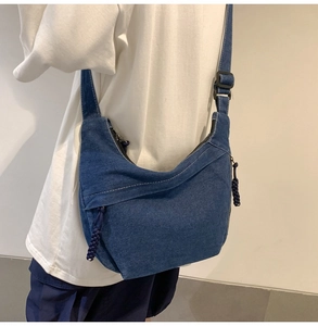 Detail of blue denim hobo bag with top stitching, decorative pockets and woven zip puller