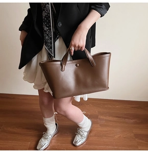 Close-up of a brown leather tote bag showing fine texture and snap button detail