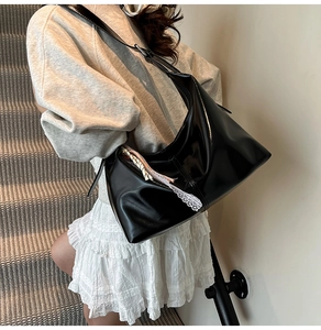 Detail of black patent hobo bag with lace trim and adjustable strap worn by model